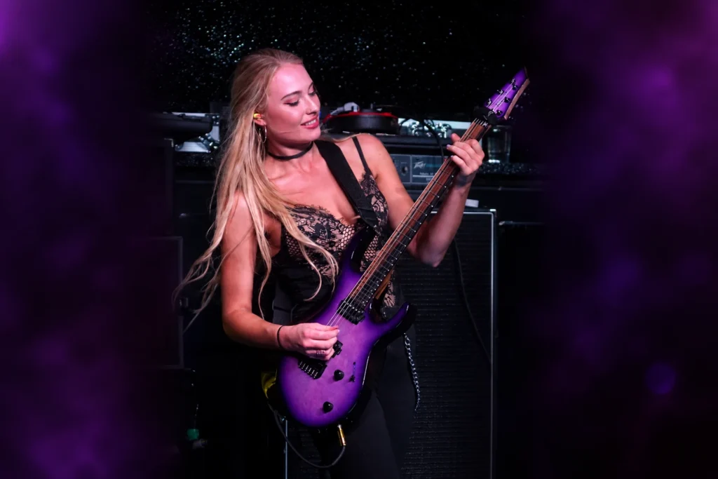 Sophie Lloyd performing live on stage with a purple electric guitar.