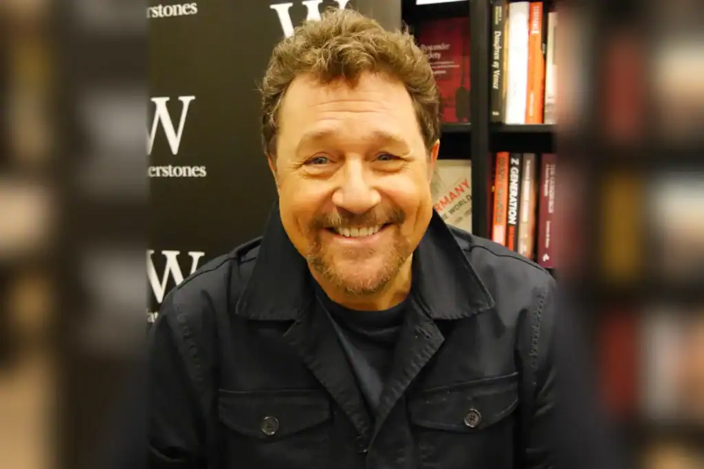 Michael Ball smiling in a dark jacket, with bookshelves and a Waterstones backdrop behind him.